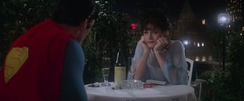 Movie still from “Superman” (1978), directed by Richard Donner – A woman sitting at a table with a glass of wine; Medium shot, Over the shoulder angle