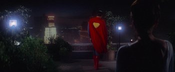 Movie still from “Superman” (1978), directed by Richard Donner – A man in a superman costume stands on the sidewalk; Wide shot, Low angle
