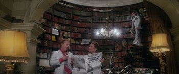 Movie still from “Superman” (1978), directed by Richard Donner – A man and a woman holding a newspaper in a room full of bookshelves; Wide shot, High angle