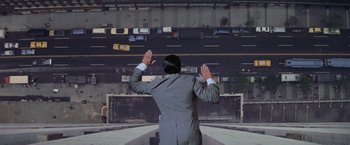 Movie still from “Superman” (1978), directed by Richard Donner – A man in a gray suit is holding his hands in the air; Wide shot, Overhead angle
