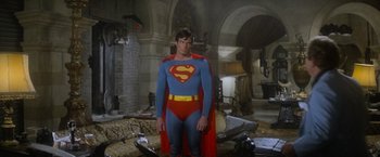 Movie still from “Superman” (1978), directed by Richard Donner – A man in a superman costume standing in a room; Wide shot, Over the shoulder angle