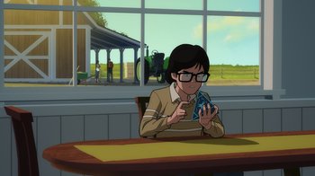 Movie still from “Superman: Man of Tomorrow” (2020), directed by Chris Palmer – A man sitting at a table with a cell phone in front of him; Medium shot, Over the shoulder angle