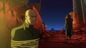 Movie still from “Superman: Man of Tomorrow” (2020), directed by Chris Palmer – A man with a rope around his neck is standing in front of some rocks; Wide shot, Over the shoulder angle