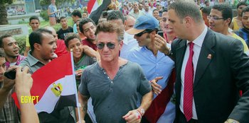 Movie still from “Superpower” (2023), directed by Aaron Kaufman – A group of people gathered around a man in a crowd; Medium shot, Over the shoulder angle