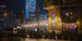 Movie still from “Superpower” (2023), directed by Aaron Kaufman – People are walking on the sidewalk near a building; Extreme Wide shot, Low angle