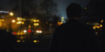Movie still from “Superpower” (2023), directed by Aaron Kaufman – A man standing in front of a street at night; Medium shot, Over the shoulder angle