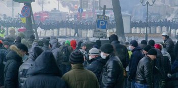 Movie still from “Superpower” (2023), directed by Aaron Kaufman – A group of people standing in front of a line of police officers; Wide shot, High angle
