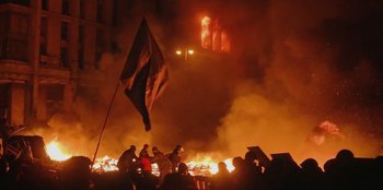 Movie still from “Superpower” (2023), directed by Aaron Kaufman – A group of people standing around a burning building; Extreme Wide shot, High angle