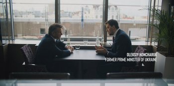 Movie still from “Superpower” (2023), directed by Aaron Kaufman – Two men sitting at a table in front of each other; Medium shot, Over the shoulder angle