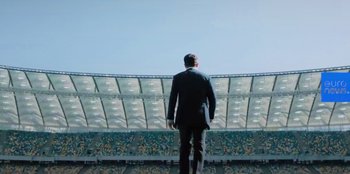 Movie still from “Superpower” (2023), directed by Aaron Kaufman – A man in a suit stands in front of an empty stadium; Wide shot, Low angle