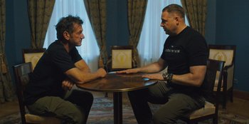 Movie still from “Superpower” (2023), directed by Aaron Kaufman – A couple of men sitting at a round table; Medium shot, Over the shoulder angle