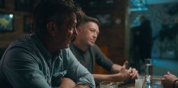 Movie still from “Superpower” (2023), directed by Aaron Kaufman – A couple of men sitting at a wooden table; Medium shot, Over the shoulder angle