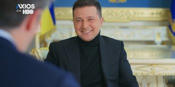 Movie still from “Superpower” (2023), directed by Aaron Kaufman – A man in a black suit smiling for the camera; Close Up shot, Low angle