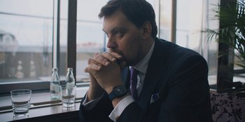 Movie still from “Superpower” (2023), directed by Aaron Kaufman – A person wearing a suit and tie; Close Up shot, Low angle