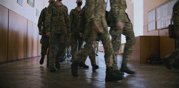 Movie still from “Superpower” (2023), directed by Aaron Kaufman – A group of soldiers walking down a hall way; Wide shot, High angle