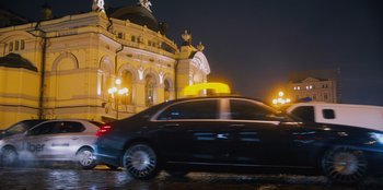 Movie still from “Superpower” (2023), directed by Aaron Kaufman – A car driving down a street at night past a large building; Wide shot, Low angle