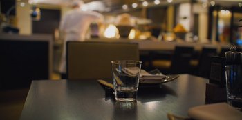 Movie still from “Superpower” (2023), directed by Aaron Kaufman – A shot glass sitting on top of a wooden table; Extreme Close Up shot, High angle