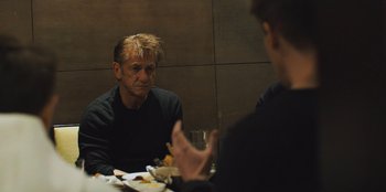 Movie still from “Superpower” (2023), directed by Aaron Kaufman – A man sitting at a table with a glass of wine; Medium shot, Over the shoulder angle