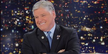 Movie still from “Superpower” (2023), directed by Aaron Kaufman – A man in a suit and tie smiling for the camera; Close Up shot, Over the shoulder angle
