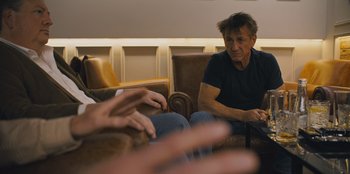 Movie still from “Superpower” (2023), directed by Aaron Kaufman – A man sitting in a chair with another man; Medium shot, Over the shoulder angle