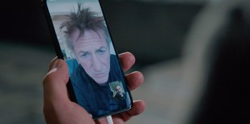 Movie still from “Superpower” (2023), directed by Aaron Kaufman – A person holding up a cell phone with a picture of a man on it; Close Up shot, High angle