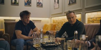 Movie still from “Superpower” (2023), directed by Aaron Kaufman – A couple of men sitting at a table with drinks; Medium shot, High angle