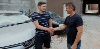 Movie still from “Superpower” (2023), directed by Aaron Kaufman – Two men shaking hands in front of a white car; Wide shot, Over the shoulder angle