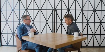 Movie still from “Superpower” (2023), directed by Aaron Kaufman – Two men sitting at a table with coffee cups; Medium shot, Over the shoulder angle