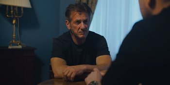 Movie still from “Superpower” (2023), directed by Aaron Kaufman – A man sitting at a table with his arms crossed; Close Up shot, Over the shoulder angle