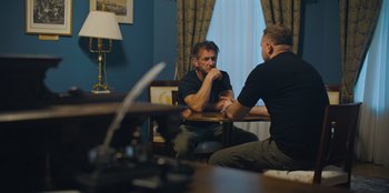 Movie still from “Superpower” (2023), directed by Aaron Kaufman – Two men sitting at a table talking to each other; Medium shot, Over the shoulder angle