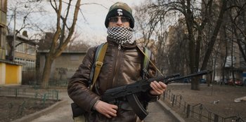 Movie still from “Superpower” (2023), directed by Aaron Kaufman – A man holding a gun wearing a leather jacket; Medium shot, Low angle