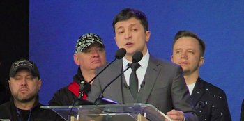Movie still from “Superpower” (2023), directed by Aaron Kaufman – A man standing at a podium speaking into microphones; Close Up shot, Low angle