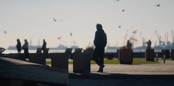 Movie still from “Superpower” (2023), directed by Aaron Kaufman – A man walking down a sidewalk next to some benches; Wide shot, Low angle
