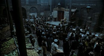 Movie still from “Sweeney Todd: The Demon Barber of Fleet Street” (2007), directed by Tim Burton – A crowd of people standing around a building; Extreme Wide shot, High angle