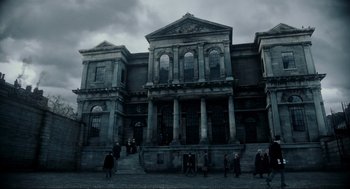 Movie still from “Sweeney Todd: The Demon Barber of Fleet Street” (2007), directed by Tim Burton – People are walking in front of an old building; Extreme Wide shot, Low angle