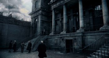 Movie still from “Sweeney Todd: The Demon Barber of Fleet Street” (2007), directed by Tim Burton – Two people in black coats walking in front of a building; Extreme Wide shot, Low angle