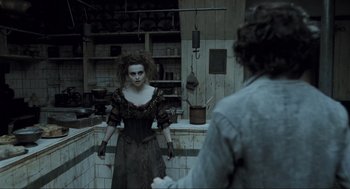 Movie still from “Sweeney Todd: The Demon Barber of Fleet Street” (2007), directed by Tim Burton – A woman standing in a kitchen holding a knife; Medium shot, Over the shoulder angle