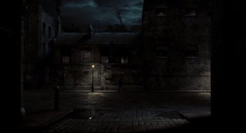 Movie still from “Sweeney Todd: The Demon Barber of Fleet Street” (2007), directed by Tim Burton – A street light on a brick sidewalk near a building at night; Extreme Wide shot, High angle