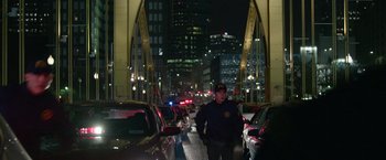 Movie still from “Sweet Girl” (2021), directed by Brian Andrew Mendoza – A police officer standing on the side of a busy street; Wide shot, Over the shoulder angle