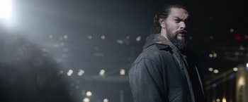 Movie still from “Sweet Girl” (2021), directed by Brian Andrew Mendoza – A man with long hair is standing in the dark; Close Up shot, Over the shoulder angle