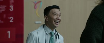 Movie still from “Sweet Girl” (2021), directed by Brian Andrew Mendoza – A man in a white shirt and a green neck tie smiling; Medium shot, Low angle