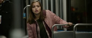 Movie still from “Sweet Girl” (2021), directed by Brian Andrew Mendoza – A woman in a pink jacket is standing on a bus; Medium shot, Over the shoulder angle