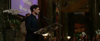 Movie still from “Sweet Girl” (2021), directed by Brian Andrew Mendoza – A man standing at a podium speaking into a microphone; Medium shot, Over the shoulder angle