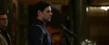 Movie still from “Sweet Girl” (2021), directed by Brian Andrew Mendoza – A man in a suit is speaking into a microphone; Close Up shot, Over the shoulder angle