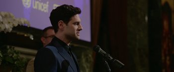 Movie still from “Sweet Girl” (2021), directed by Brian Andrew Mendoza – A man standing at a podium with a microphone in front of him; Close Up shot, Low angle