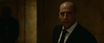 Movie still from “Sweet Girl” (2021), directed by Brian Andrew Mendoza – A man in a suit and tie in a dark room; Close Up shot, Low angle