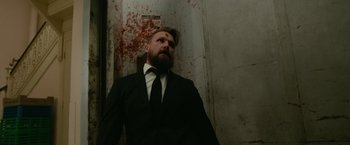 Movie still from “Sweet Girl” (2021), directed by Brian Andrew Mendoza – A man in a suit and tie standing in front of a wall; Medium shot, Low angle