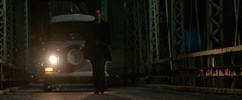 Movie still from “Sweet Girl” (2021), directed by Brian Andrew Mendoza – A man holding a gun while standing next to a car on the street; Wide shot, Low angle