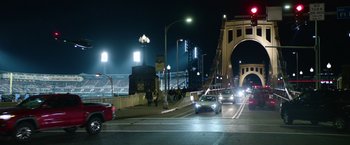 Movie still from “Sweet Girl” (2021), directed by Brian Andrew Mendoza – Cars are driving down a street at night; Extreme Wide shot, High angle