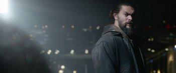 Movie still from “Sweet Girl” (2021), directed by Brian Andrew Mendoza – A man with long hair is standing in the dark; Close Up shot, Over the shoulder angle